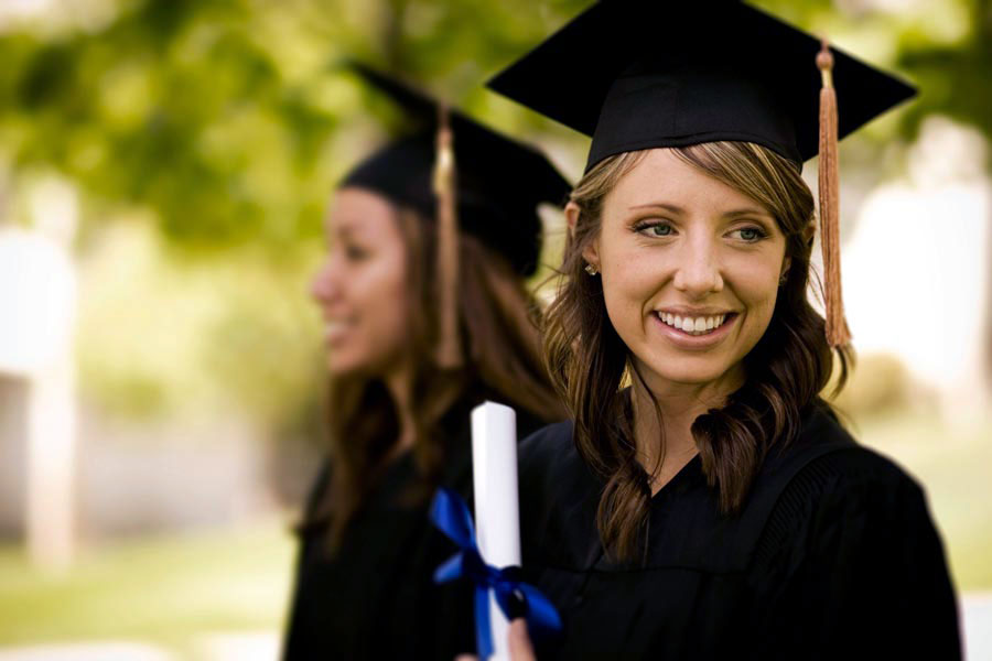 2 graduating females, holding diploma in black graduation gowns