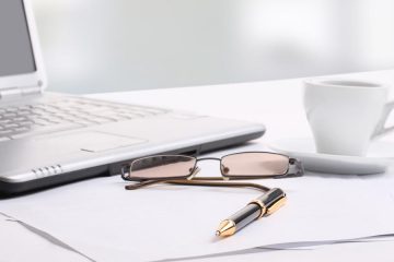glasses, cup, pen, paper and laptop on desktop